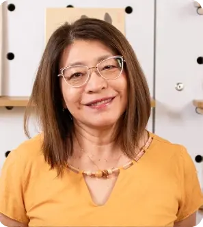 Professora Mitsuko Uehara com blusa amarela e decoração japonesa ao fundo