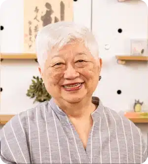 Professora Tae Suzuki sorrindo em sala decorada com elementos japoneses