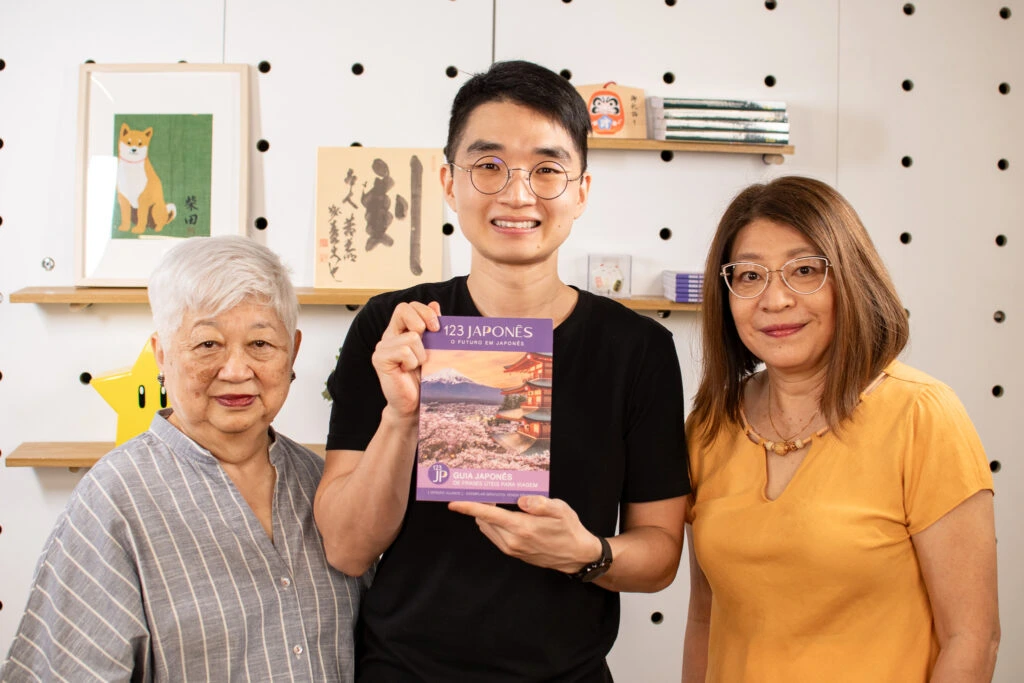 Professores do curso de japonês online 123 Japonês sorrindo e segurando o guia didático em ambiente descontraído