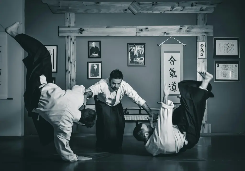 Instrutor de aikidô orientando dois praticantes que executam técnicas de queda e projeção dentro de um dojo tradicional japonês