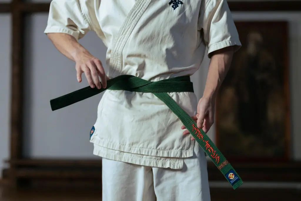 Pessoa amarrando faixa verde de karatê, em uniforme tradicional japonês