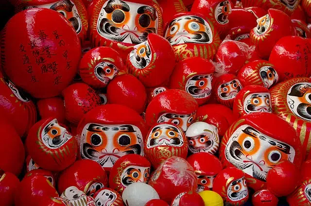 Vários bonecos Daruma vermelhos de diferentes tamanhos, amuletos japoneses associados à sorte e perseverança