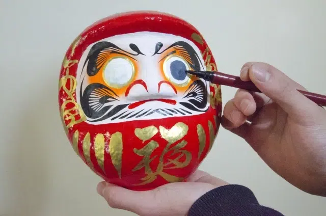 Pessoa pintando o olho de um Daruma vermelho durante o ritual japonês de realização de desejos