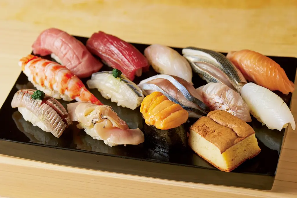 Variedade de sushi tradicional japonês servida em bandeja preta, representando a origem e o significado da palavra sushi