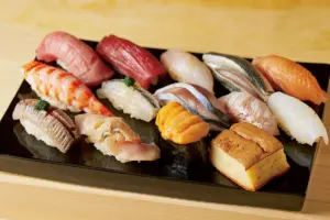 Variedade de sushi tradicional japonês servida em bandeja preta, representando a origem e o significado da palavra sushi